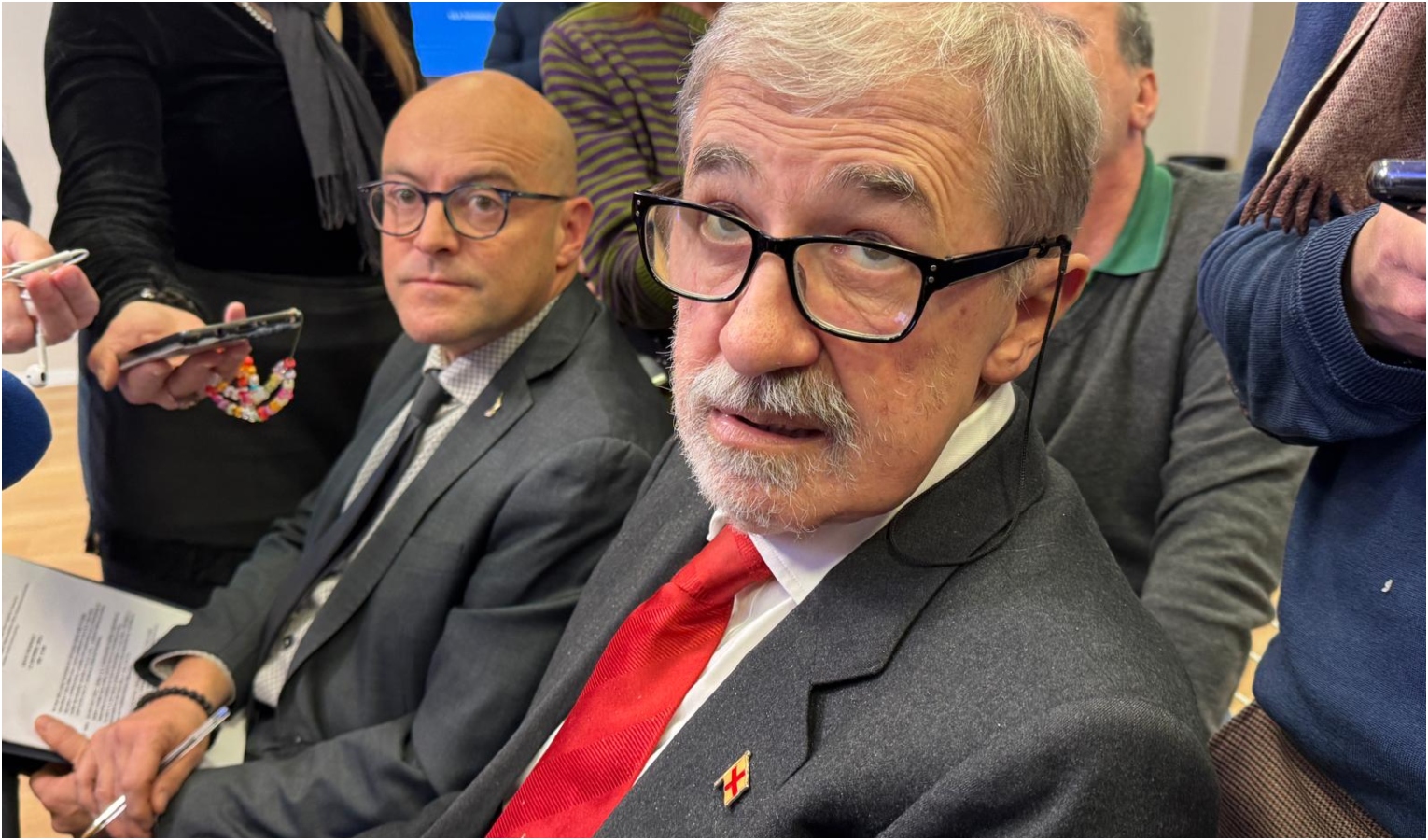 Il presidente di Regione Liguria Marco Bucci Un uomo seduto circondato da persone che lo intervistano
