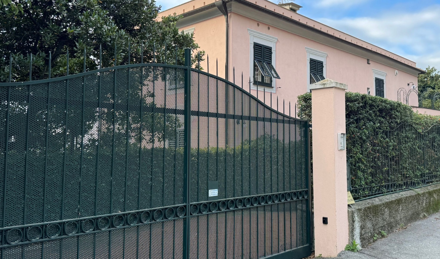 Esterno di una villa con cancello verde e palazzina rosa