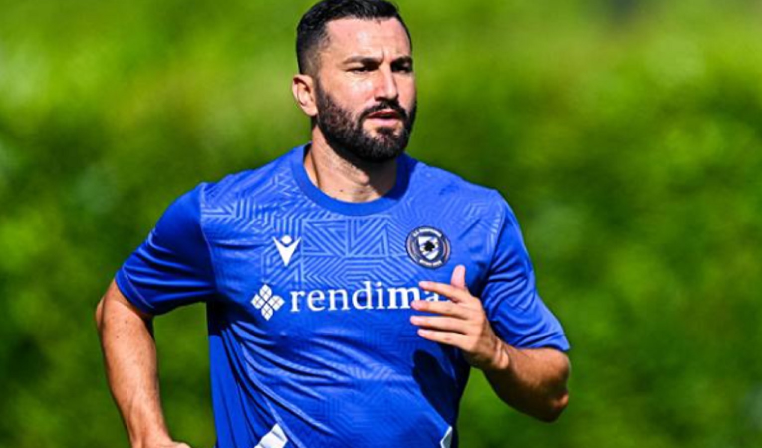 Un uomo in maglia blu, alle sue spalle del verde