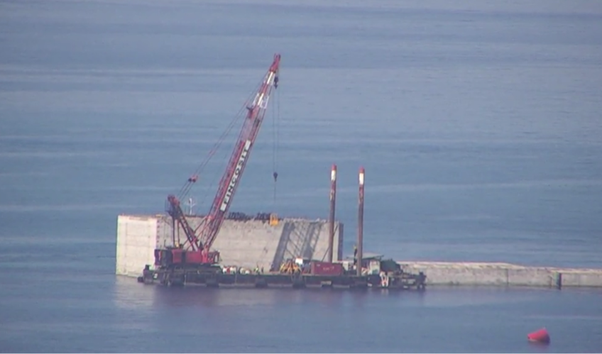 Un grosso blocco di cemento in mare con delle gru accanto 