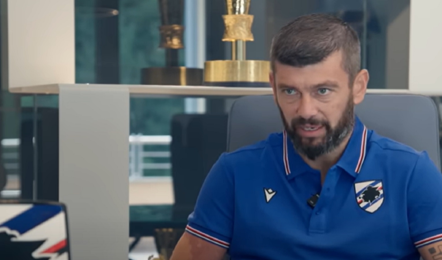 Un uomo vestito con una maglia polo della Sampdoria, è seduto e parla