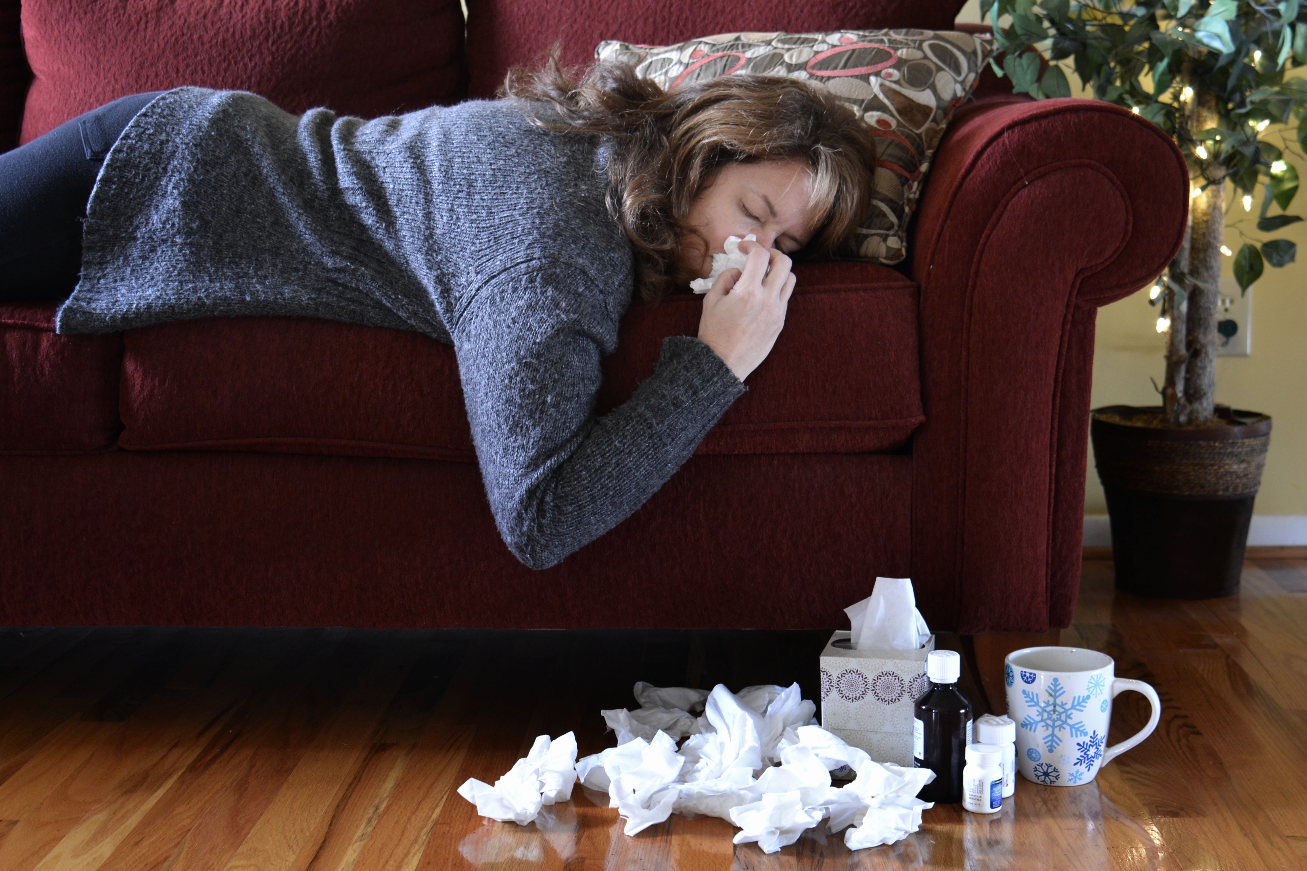 Donna con raffreddore si soffia naso su divano