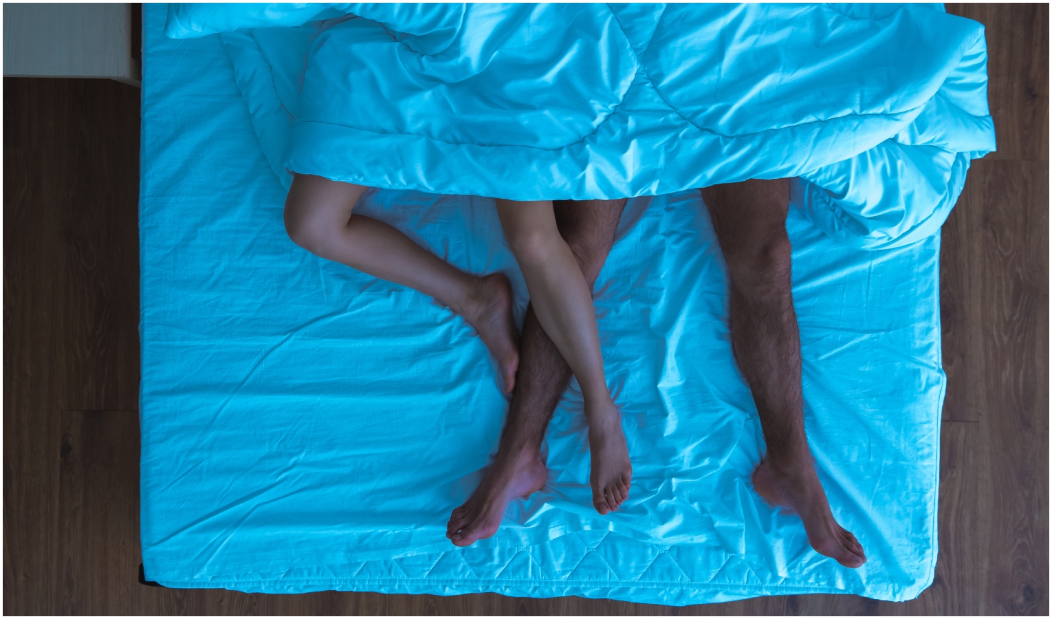 Gambe di donna e uomo sotto lenzuolo in letto