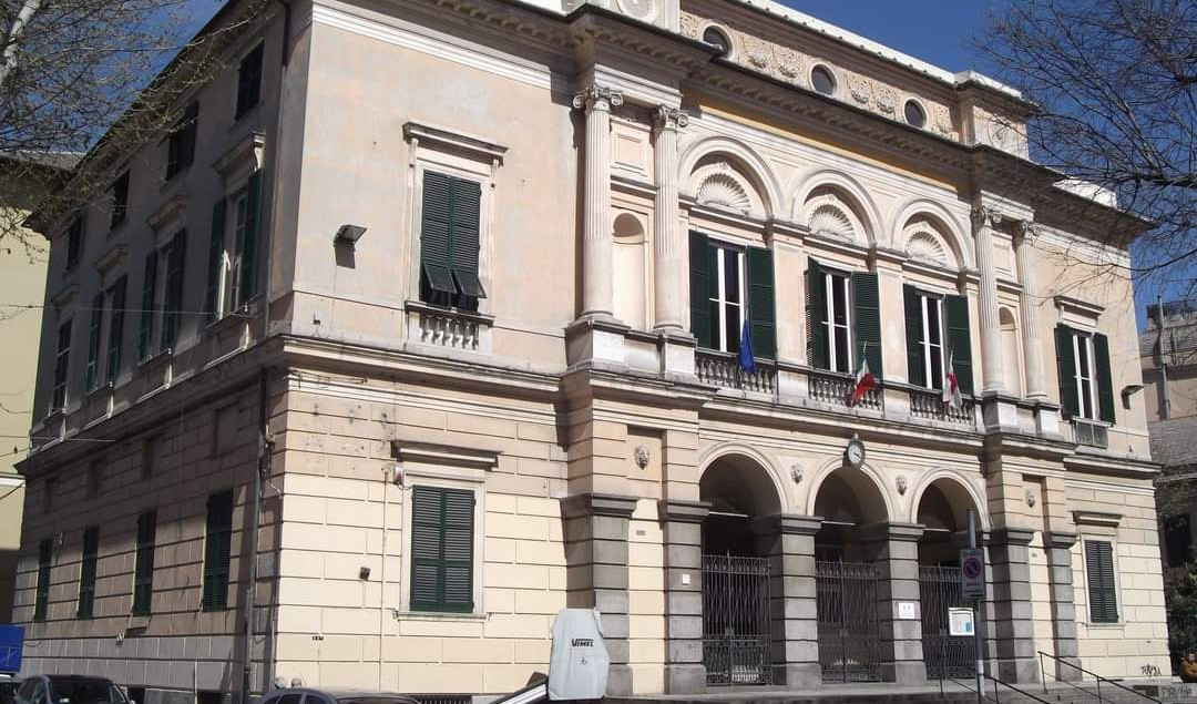 La facciata di un municipio di Genova L'esterno di un palazzo di color chiaro con finestre, persiane e bandiere esposte