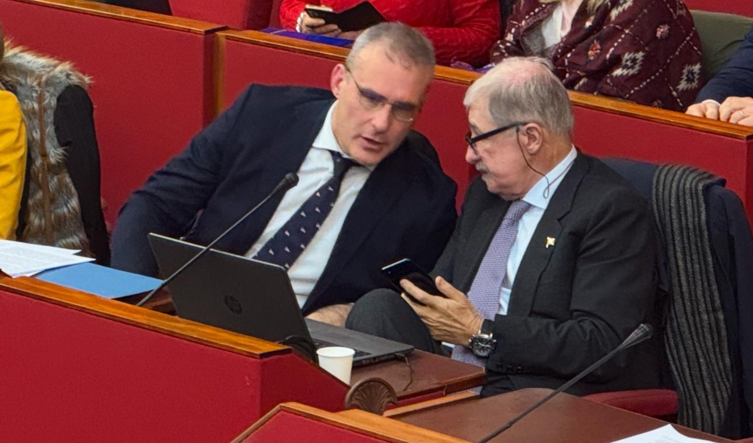 Il vicesindaco reggente di Genova Piciocchi e il presidente di Regione Liguria Bucci Due persone sedute che parlano tra loro e uno dei due mostra il cellulare