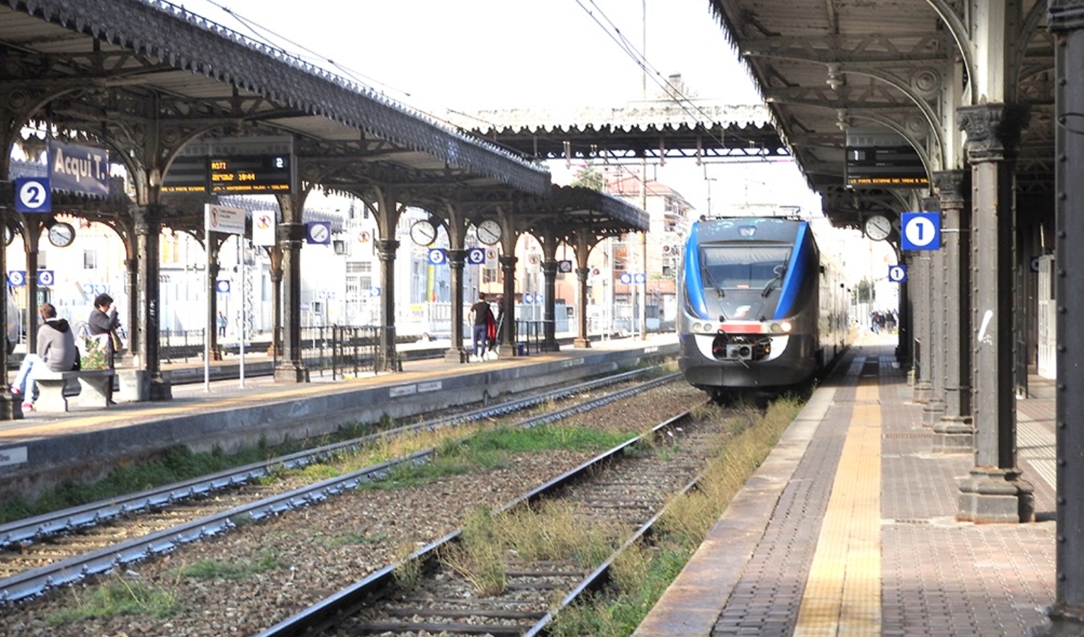 Una stazione ferroviaria in Liguria Binari di una stazione e un treno in procinto di avvicinarsi alla fermata